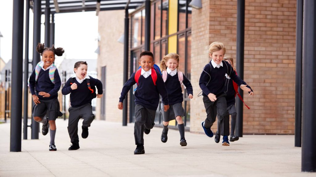 Five children in school uniform running happily outside a school building