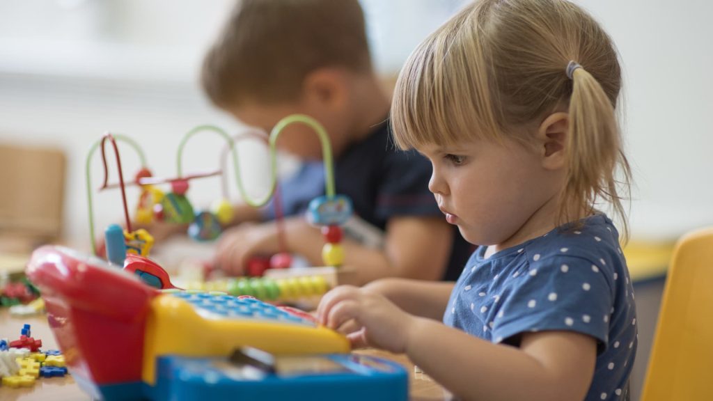 A girl of about 3 years old playing with toys on a table at nursery school